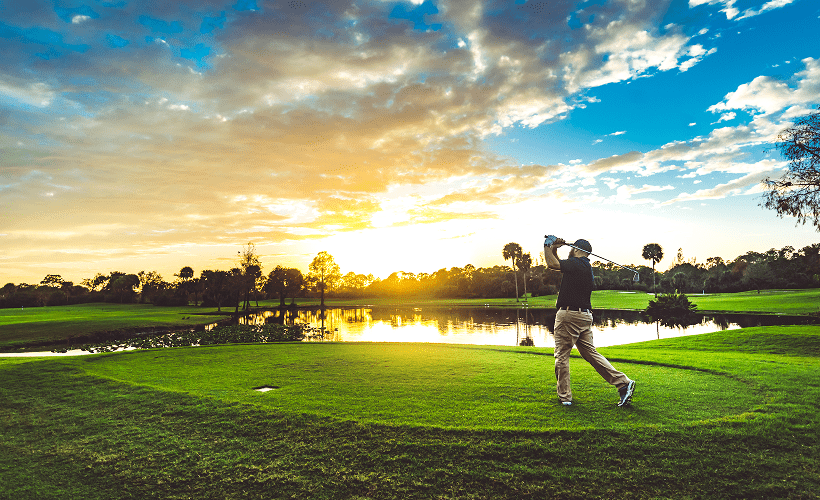 Person golfing near water at sunset